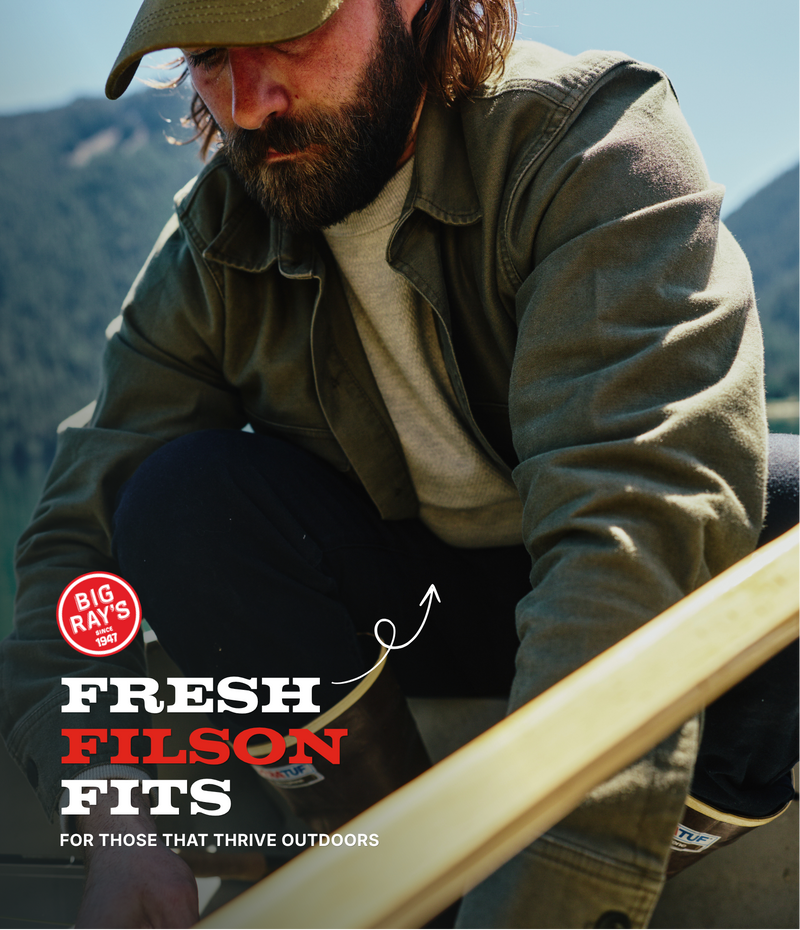 Man wearing a Filson cap and jacket with Alaska mountains in the background.
